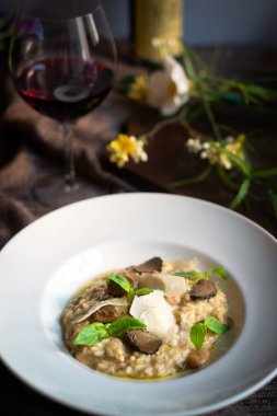 Mantarlı risotto, parmesan peyniri, fesleğen ve trüf mantarı beyaz tabakta, bir bardak şarabın yanında.
