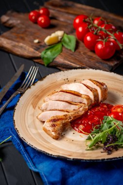 Domatesli bir tabakta kızarmış tavuk filetosu ve siyah ahşap zemin üzerinde roka. Diyet yemeği.