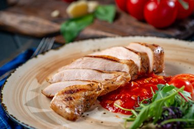 Domatesli bir tabakta kızarmış tavuk filetosu ve siyah ahşap zemin üzerinde roka. Diyet yemeği.