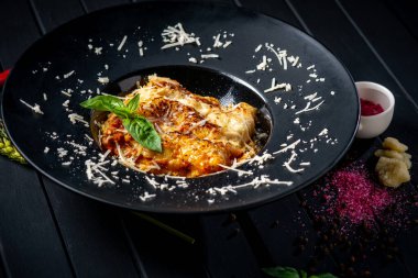 Köfte ve domates soslu et lazanyası siyah bir tabakta, ahşap arka planda. İtalyan mutfağı kavramı