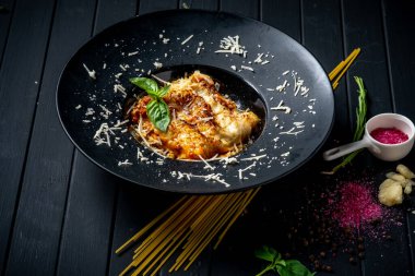 Köfte ve domates soslu et lazanyası siyah bir tabakta, ahşap arka planda. İtalyan mutfağı kavramı