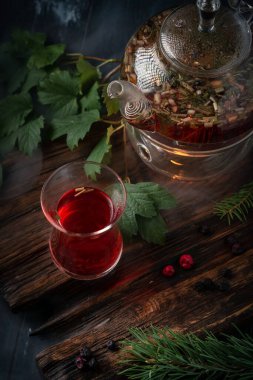 Koyu ahşap arka planda bir çaydanlıkta kuşüzümlü bir bardak bitki çayı. Yabani dutlardan mis kokulu doğal içecek.