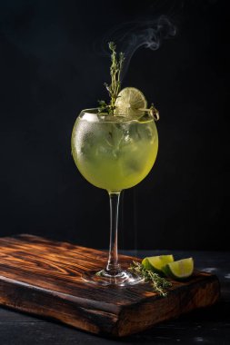 Koyu bir arka planda Basil Leaf, kireç ve buzlu bir şarap kadehiyle kokteyl tazeliyorum. Cin tonik iç.