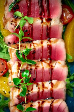 Dilimlenmiş ton balığı, yeşil salata ve ahşap bir tabakta domates. Kapat.