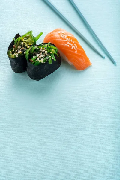 Two seaweed Sushi Chuka and sushi nigiri with salmon with chopsticks on a blue background. Copy space