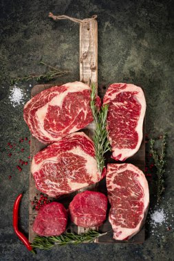 Tahta üzerinde taze çiğ biftek seti: fileto, Striploin, pirzola ve biberiye, üst manzara