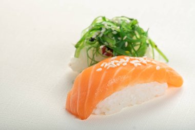 Açık bej arka planda iki farklı suşi, somon balığı ve yosun, nigiri sake ve chuka.