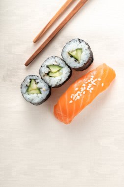 Somonlu suşi ve açık bej arka planda çubuklu salatalık, nigiri sake ve futomaki.