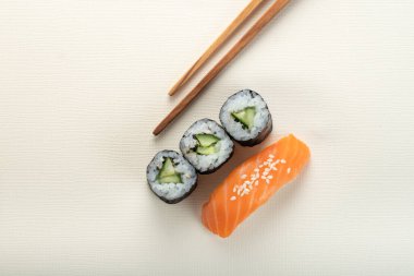 Somonlu suşi ve açık bej arka planda çubuklu salatalık, nigiri sake ve futomaki.