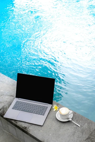 Laptop at the swimming pool with a Cup of coffee, workspace at a freelancer on vacation