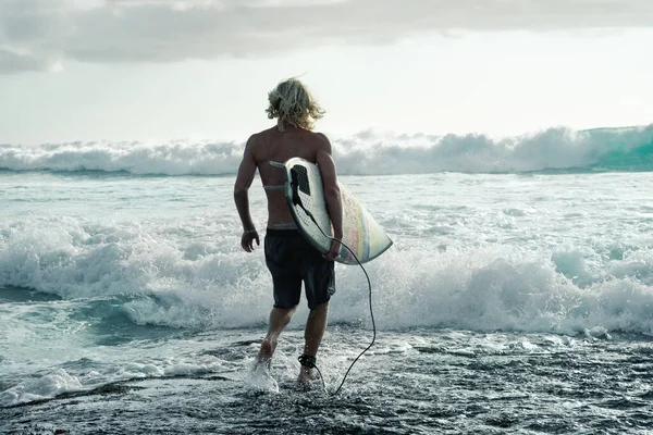 Male surfer with a short Board goes into the ocean with big waves, lifestyle on the coast