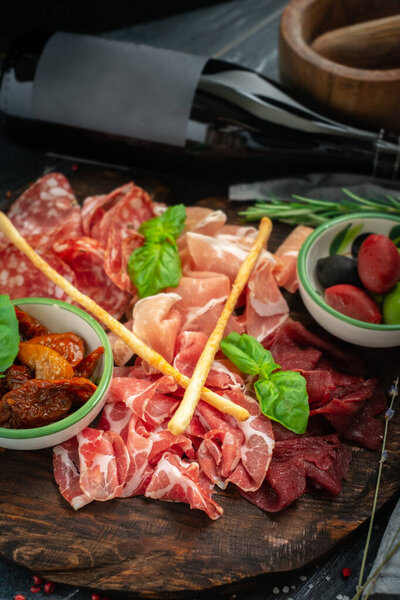Italian meat appetizers and wine on a wooden tray. Wine snack Antipasto-salami, prosciutto, slices ham, beef jerky and bread sticks.