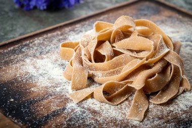 Tahta bir tahtanın üzerinde unlu kestaneli pişmemiş kahverengi makarna tagliatelle.