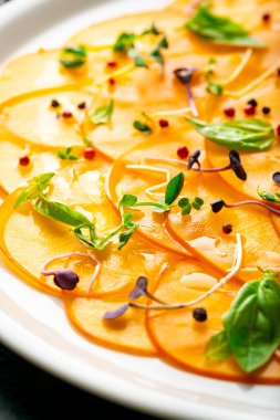 Beyaz tabakta yeşil yapraklarla dilimlenmiş tatlı hurma salatası.