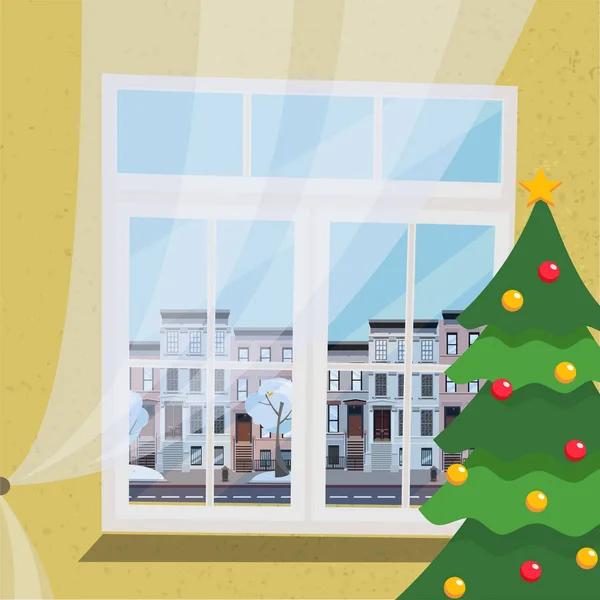 A new-year flat interior with a decorated Christmas tree, standing next to a large white plastic window with a drawn tulle with a view of the city's elegant landscape, low-rise apartment buildings.