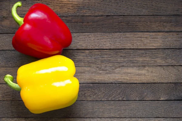 Red and yellow sweet peppers on wooden table with copy space