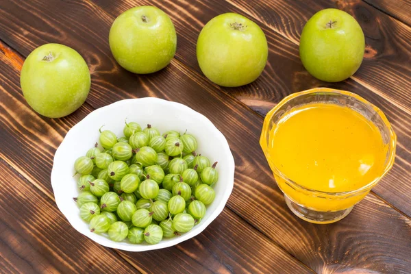 Yummy raw diet. Green apples, gooseberries and sweet yellow honey on dark wooden table.
