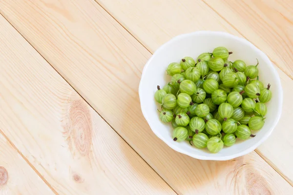 Healthy snack for raw diet. Green gooseberries on wooden background with copy space. Top view.