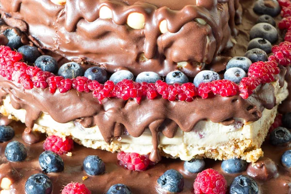 Close up raw healthy vegan cheesecake with chocolate, raspberries, blueberries and nuts. Raw diet.