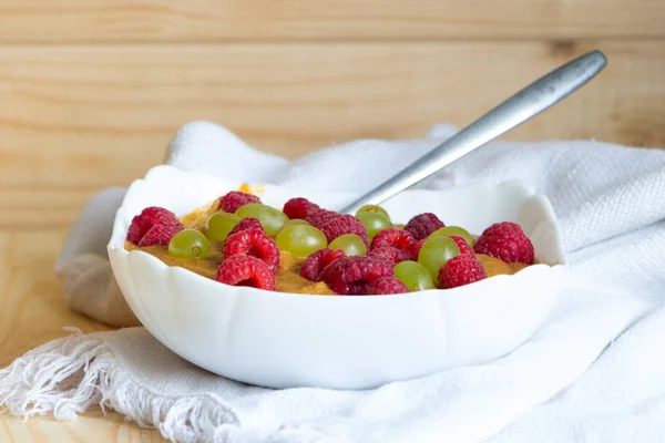 Healthy raw food diet breakfast. Flaxseed porridge with grapes and raspberries in white bowl.