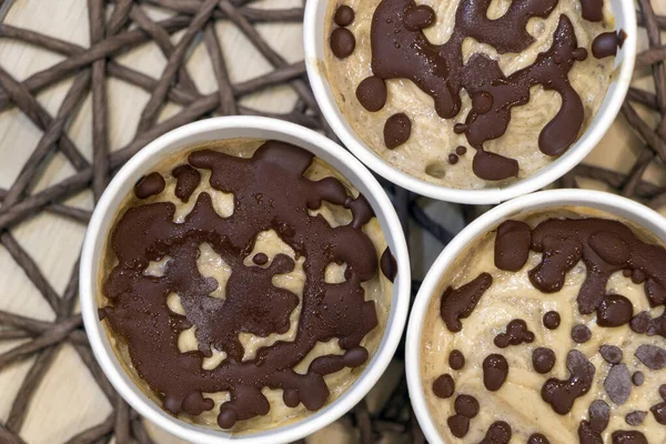 Healthy vegan sweet dessert. Raw banana ice cream with coconut cream coated with natural chocolate droplets in a white paper cups on table covered with wicker tablecloth. Copy space. Top view