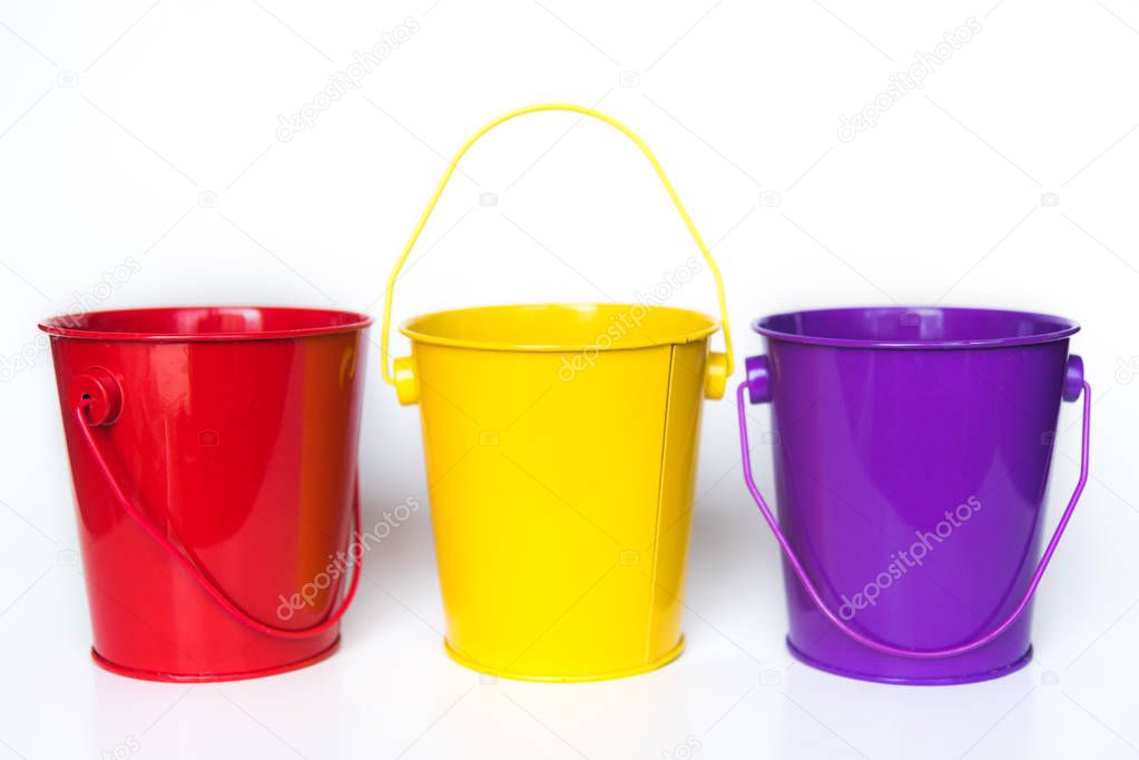 Three metal buckets colored red, yellow, and purple standing in row against solid white background