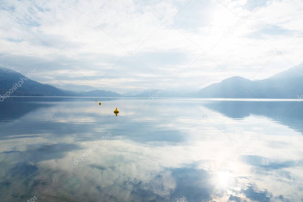Clouds, fog, sunshine, and mountains reflected in calm lake