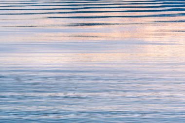 Gökyüzü, mor, pembe ve mavi renklerde günbatımında yansıtan göl yüzeyi yumuşak dalgalanmalar
