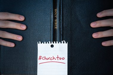 Kapağında #churchtoo hashtag ile Kutsal Kitap tutan ellerin yakın çekim