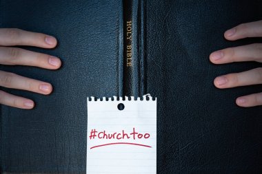 Close-up of hands holding Holy Bible with hashtag #churchtoo written on the cover clipart