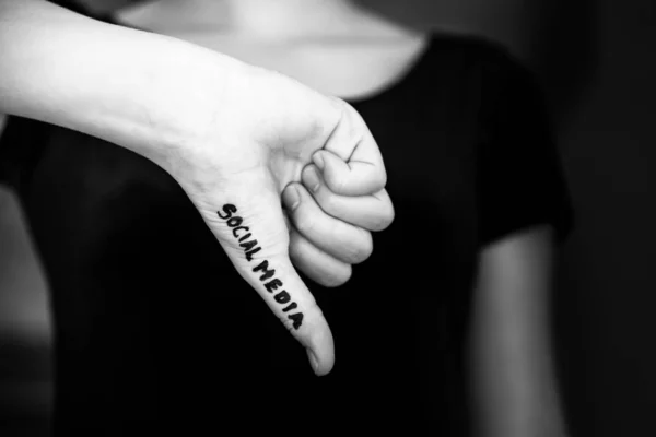 Black and white close-up of woman\'s hand making thumbs down gesture with words social media written on hand