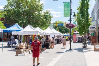 Penticton, British Columbia/Kanada - 15 Haziran 2019: Popüler bir yaz etkinliği olan Main Street'teki haftalık Penticton Community Market'te satışa sunulan çeşitli mal tablolarına insanlar göz atılmaktadır.