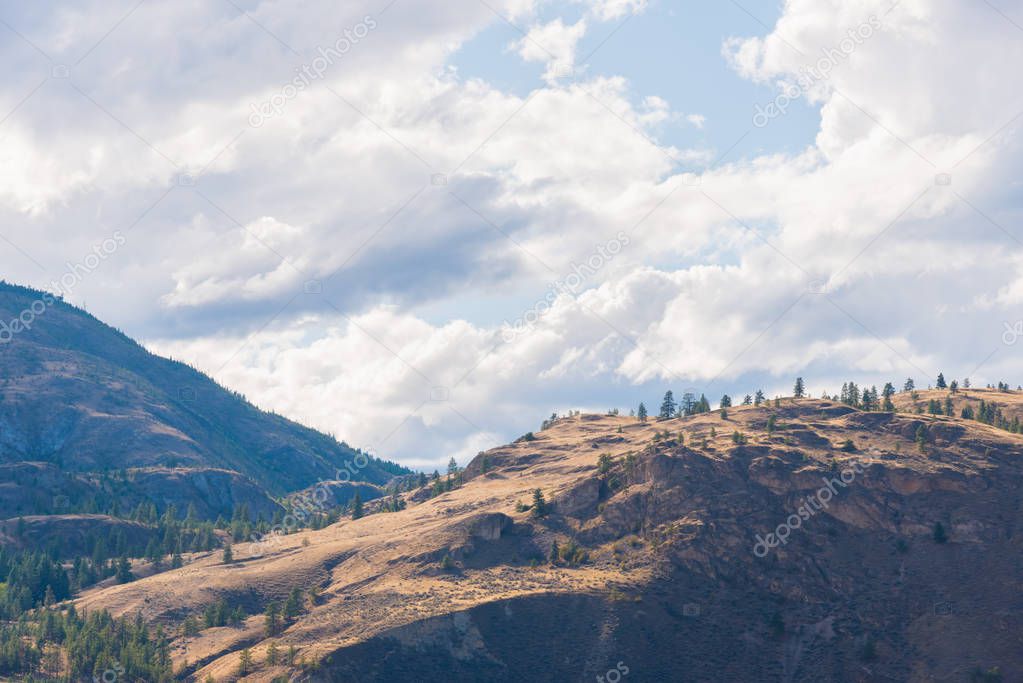 Distant hills glowing in sunlight with moody clouds and blue sky in Okanagan Valley