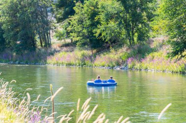 Erkek ve kadın yaz aylarında iki kişilik iç tüp üzerinde Penticton Nehri Kanalı aşağı yüzer