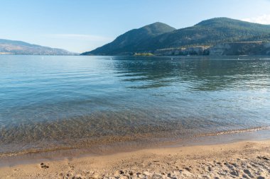 Okanagan Gölü, kum plajı, mavi gökyüzü ve yaz aylarında dağlar