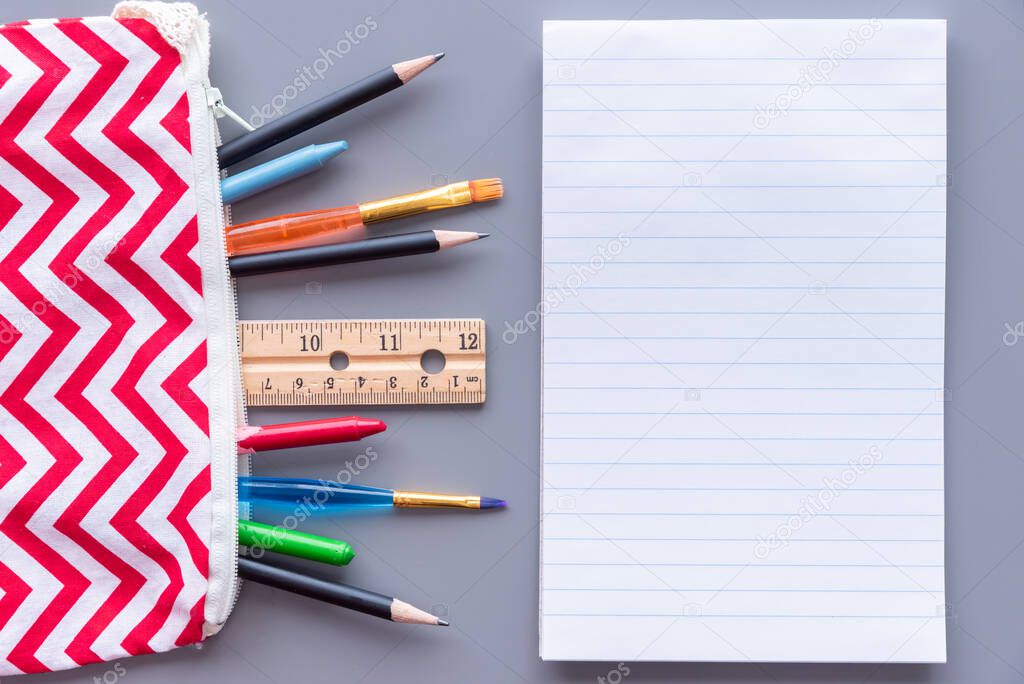 Lined paper on table beside pencil case full of stationery supplies