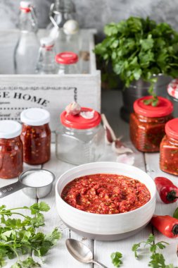 Kırmızı acı biber sıcak sos pişirme süreci. Malzemeler: biber, yeşillik, fesleğen, kırmızı biber ahşap bir masada. Hazır soslu cam kavanozlar.