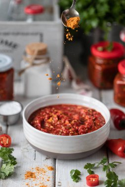 Kırmızı acı biber sıcak sos pişirme süreci. Malzemeler: biber, yeşillik, fesleğen, kırmızı biber ahşap bir masada. Hazır soslu cam kavanozlar.