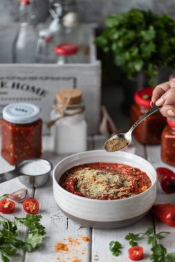 Kırmızı acı biber sıcak sos pişirme süreci. Malzemeler: biber, yeşillik, fesleğen, kırmızı biber ahşap bir masada. Hazır soslu cam kavanozlar.