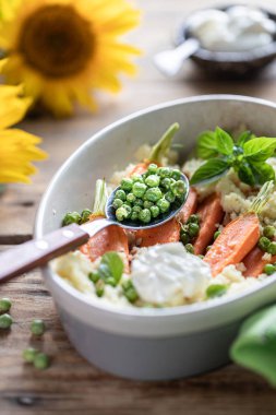 Pravanese otlar ile pişmiş genç havuç. kuskus Ekşi krema, yoğurt veya taze krema, genç yeşil bezelye. Çiçekler ayçiçeği ahşap masa