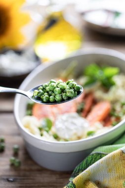 Pravanese otlar ile pişmiş genç havuç. kuskus Ekşi krema, yoğurt veya taze krema, genç yeşil bezelye. Çiçekler ayçiçeği ahşap masa