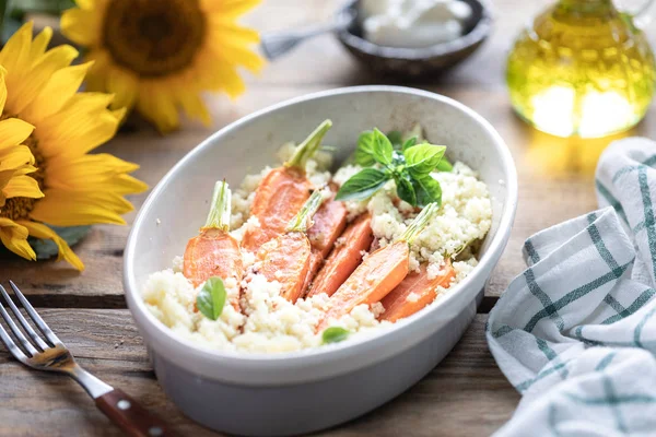 Pravanese otlar ile pişmiş genç havuç. kuskus Ekşi krema, yoğurt veya taze krema. Çiçekler ayçiçeği ahşap masa