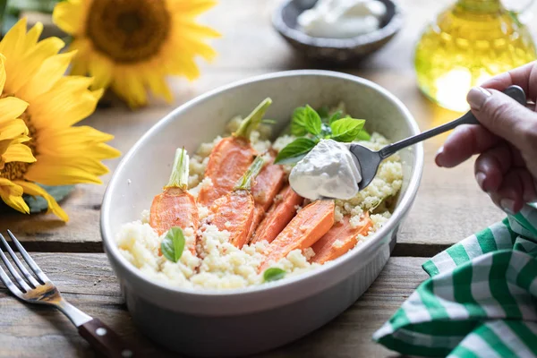 Pravanese otlar ile pişmiş genç havuç. kuskus Ekşi krema, yoğurt veya taze krema. Çiçekler ayçiçeği ahşap masa