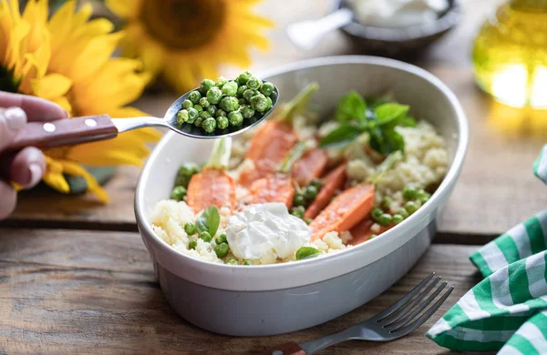 Pravanese otlar ile pişmiş genç havuç. kuskus Ekşi krema, yoğurt veya taze krema, genç yeşil bezelye. Çiçekler ayçiçeği ahşap masa