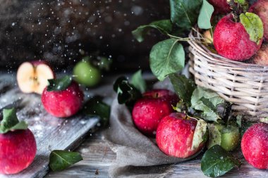 Tahta bir masanın üzerinde hasır sepetteki kırmızı elmalar, bulanık arka plan. Karanlık fotoğraf