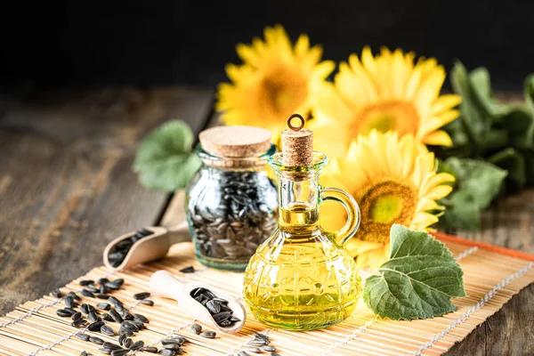 Подсолнечное масло в бутылочном стакане с семенами и цветами подсолнечника. на размытом фоне — стоковое фото