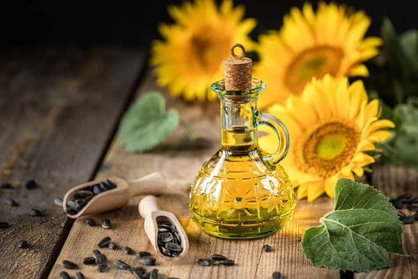 Подсолнечное масло в бутылочном стакане с семенами и цветами подсолнечника. на размытом фоне — стоковое фото