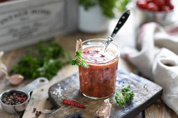 The process of making hot red tomato sauce. Ingredients: tomato, herbs, basil, paprika on a wooden table. Glass jars with ready-made sauce — Stock Photo, Image