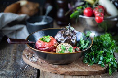 Fırında patlıcan veya patlıcan domuz eti ve sığır eti, biber, domates ve taze maydanoz ile ahşap bir masa üzerinde siyah bir tabak ta dolması