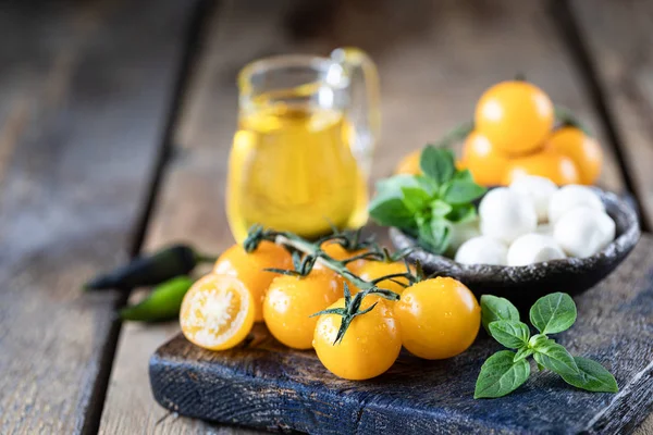 Mozzarella, pomodori gialli e basilico in una ciotola di ceramica su una tavola di legno. Olio d'oliva. Ingredienti per insalata Caprese. Focus selettivo — Foto Stock